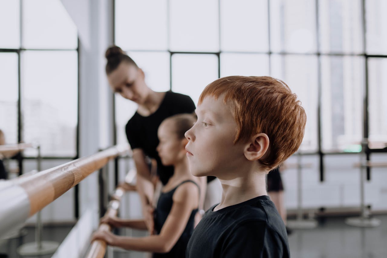 Young ballet students practicing at the barre in a sunlit studio with their instructor.